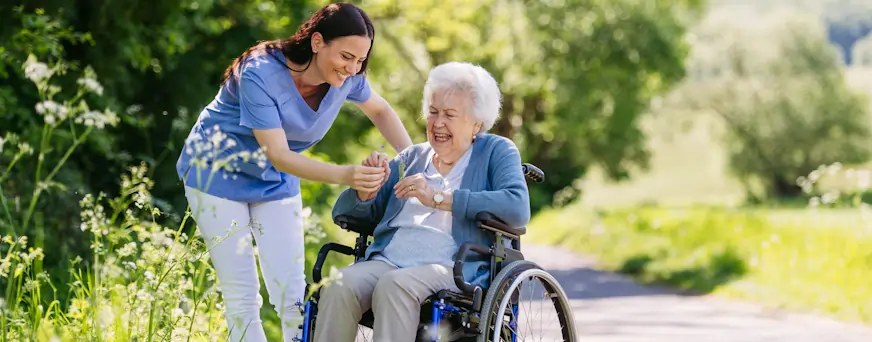 Life Assure Senior Woman In Wheelchair With Caregiver At Park Hero